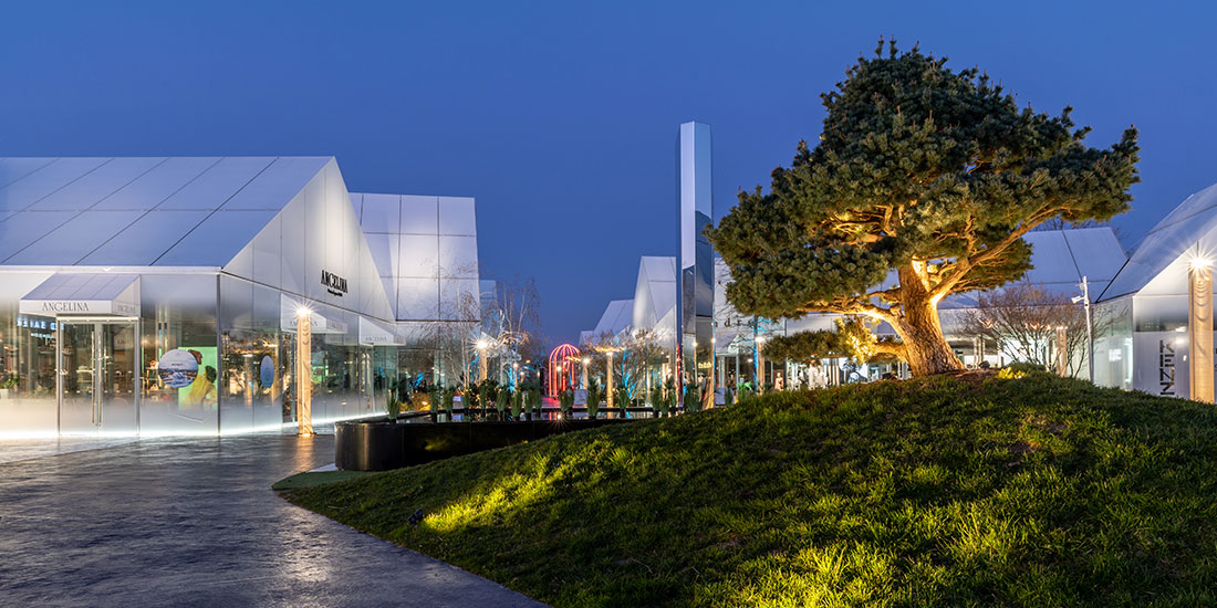 Architecture extérieure du Village des Marques de Villefontaine éclairée de nuit, avec boutiques contemporaines et aménagement paysager