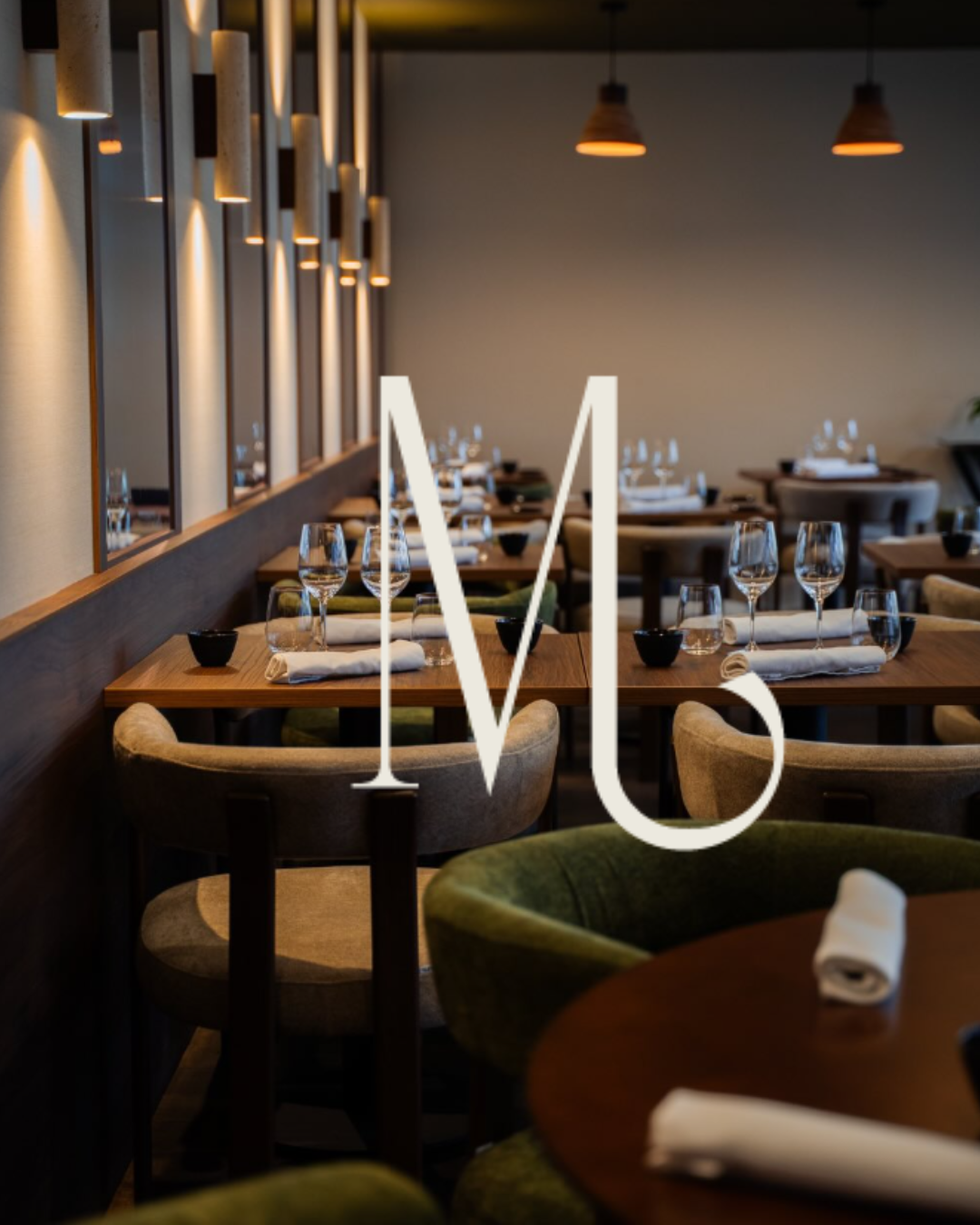 Salle à manger du restaurant Mensa à Tours, tables dressées et fauteuils velours vert, monogramme M en surimpression