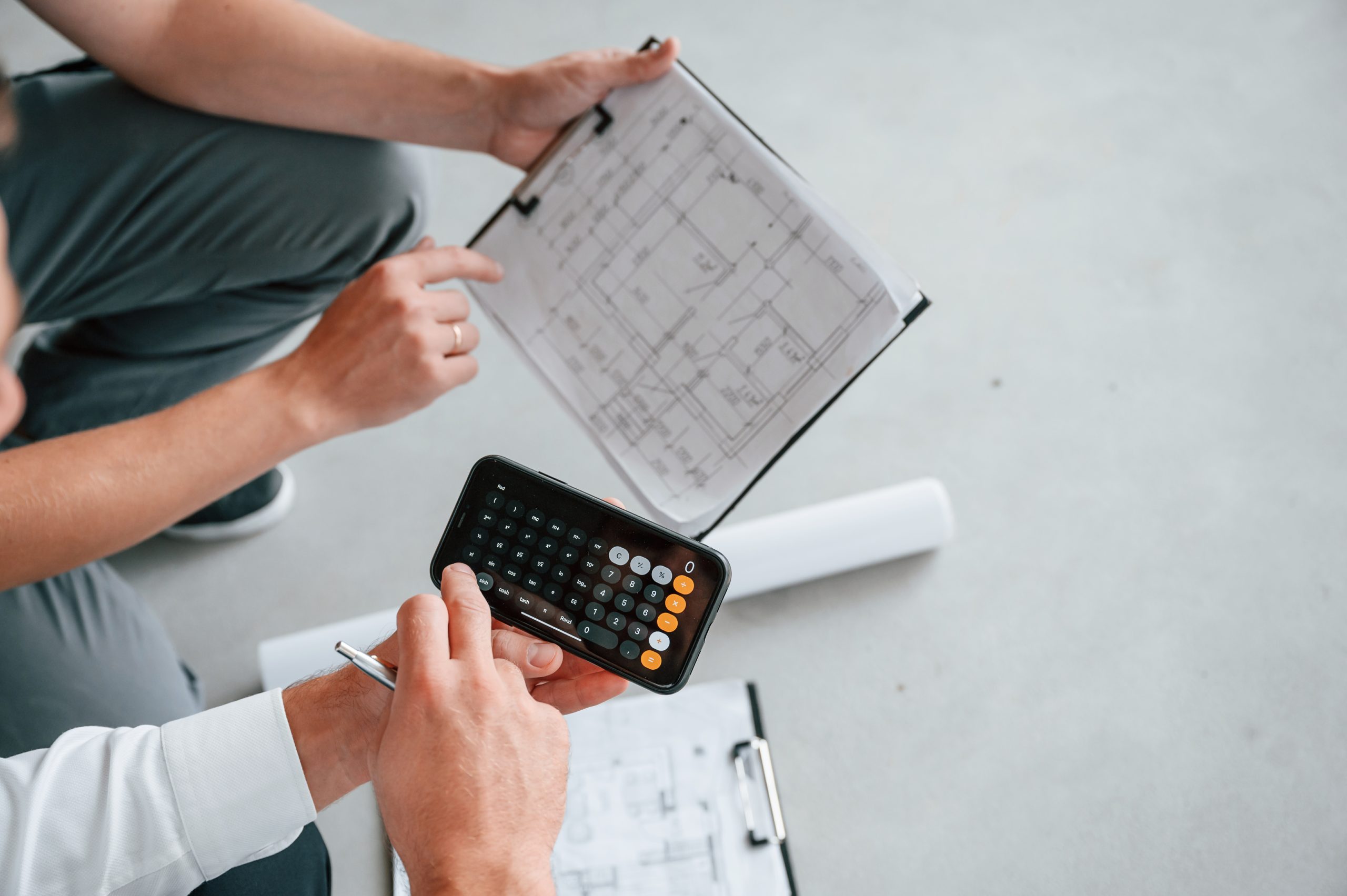 Architecte notant des estimations budgétaires sur un plan avec calculatrice