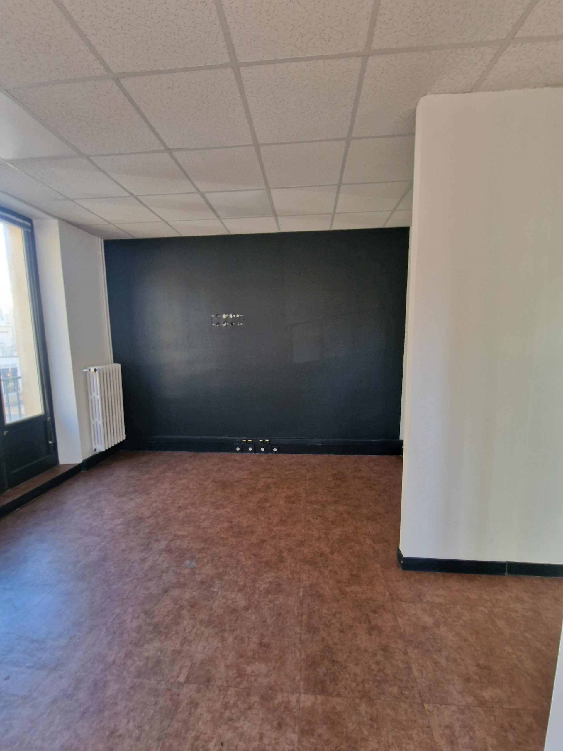 Pièce vide avant rénovation avec pan de mur foncé, radiateur et sol vinyle marron, futur restaurant Table à Blois