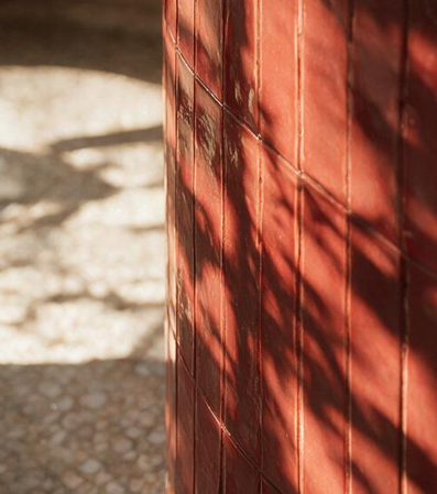 Colonne habillée de zellige rouge avec ombres portées de feuillage sur sol en terrazzo au restaurant Table