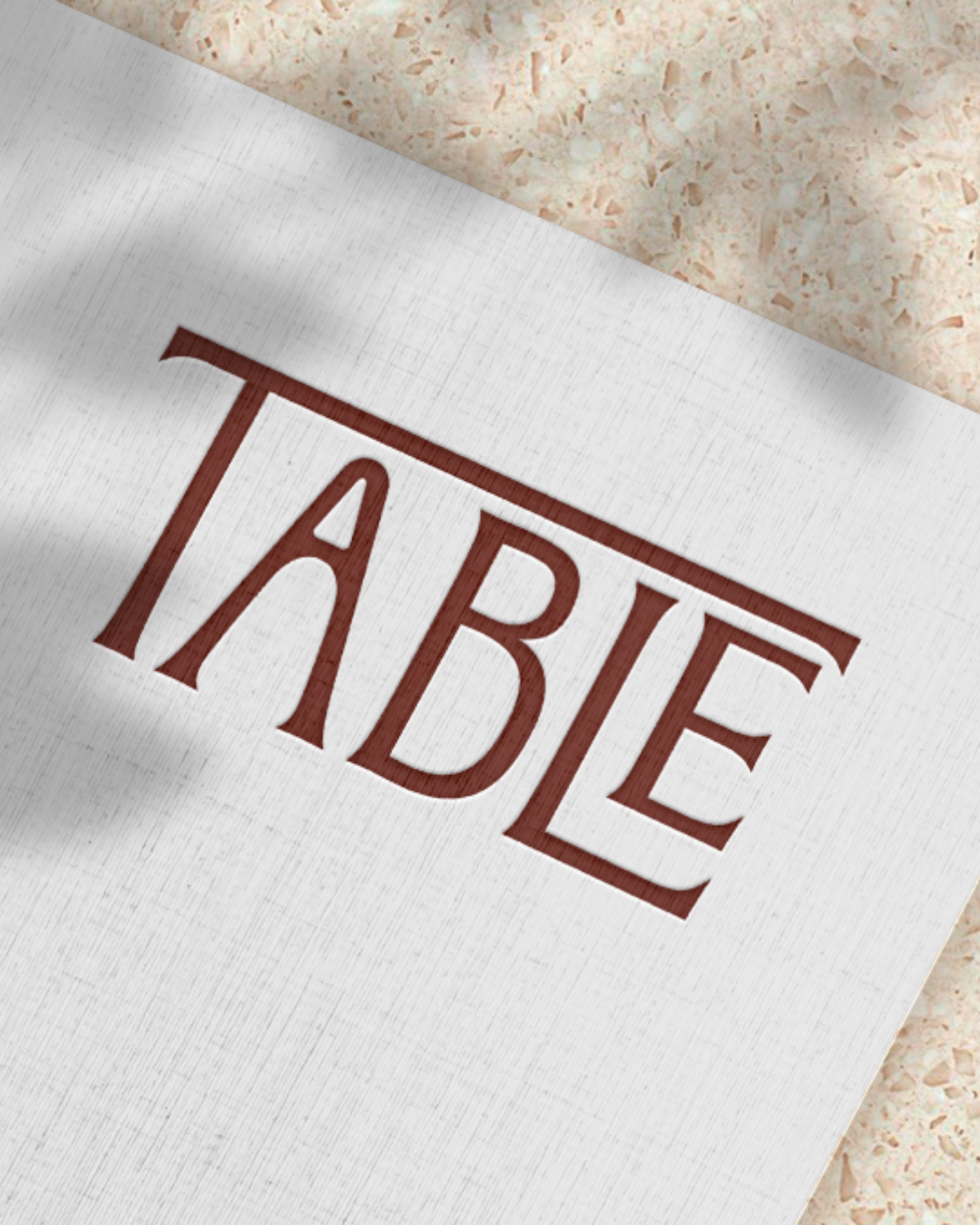 Logo Table gravé en relief sur papier texturé, mockup d'identité visuelle sur fond terrazzo