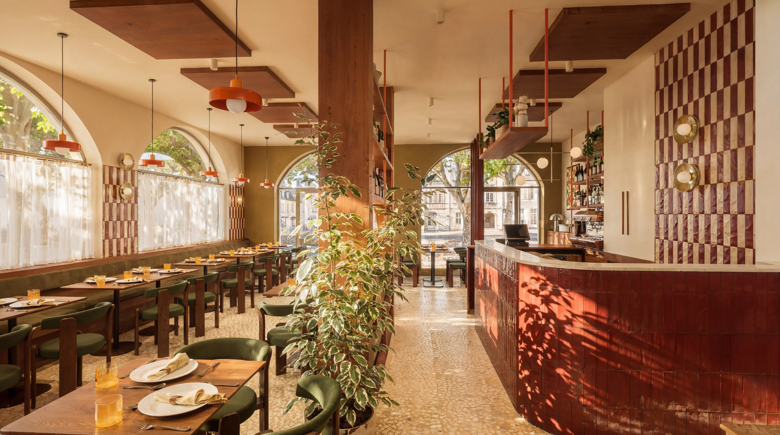 Salle du restaurant Table à Blois avec comptoir en zellige rouge, banquette verte et fenêtres en arc éclairées par des suspensions orange
