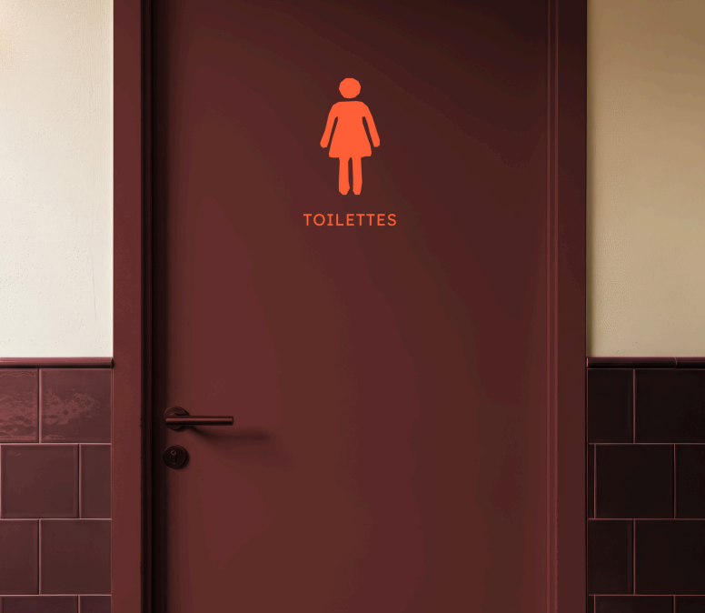 Pictogramme signalétique orange femme sur porte bordeaux des toilettes, avec carrelage assorti au restaurant Table